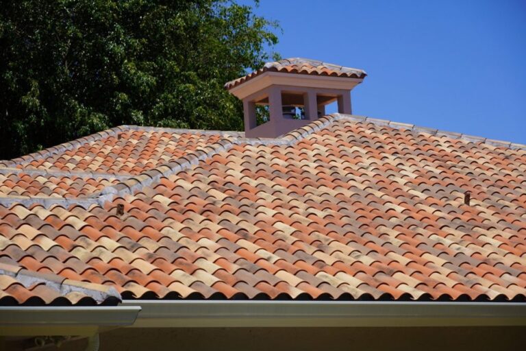 Close-up of a Mediterranean-style roof featuring red, orange, and sand-coloured clay barrel tiles under a blue sky.