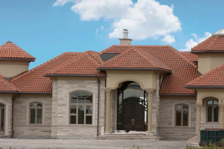 Elegant Mediterranean-style stone home with red clay roof tiles under a blue sky.